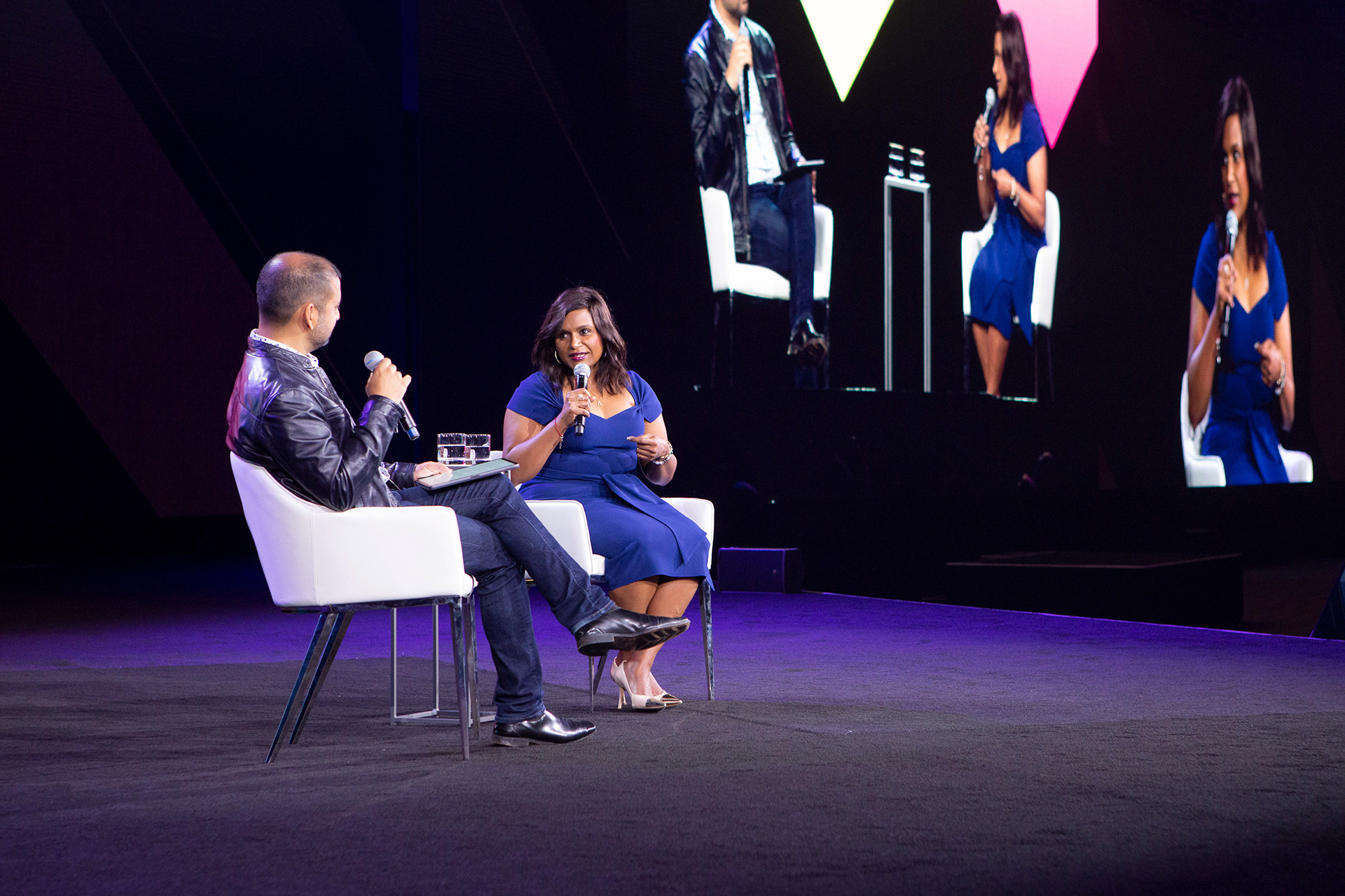 Full-stage shot of two-person fireside chat with audience visible in foreground
